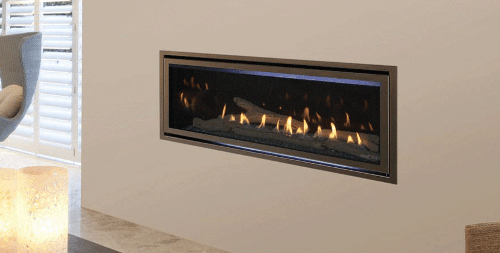 Long rectangular electric fireplace, lit, in white wall of a home.
