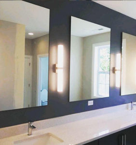Row of three rectangular un-framed mirrors in a bathroom, over a white vanity, on a dark blue wall.
